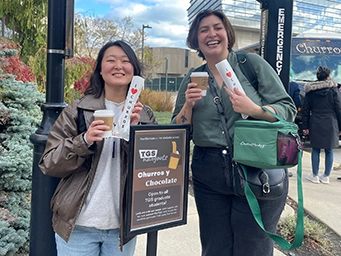 two students holding up I love churros and drinks outside